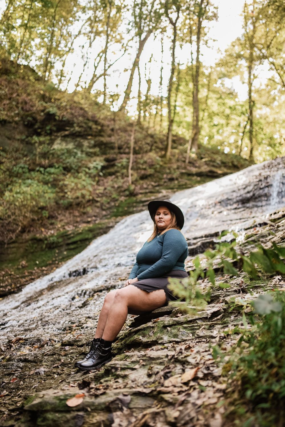 Person in blue top and hat poses on rocky waterfall slope.