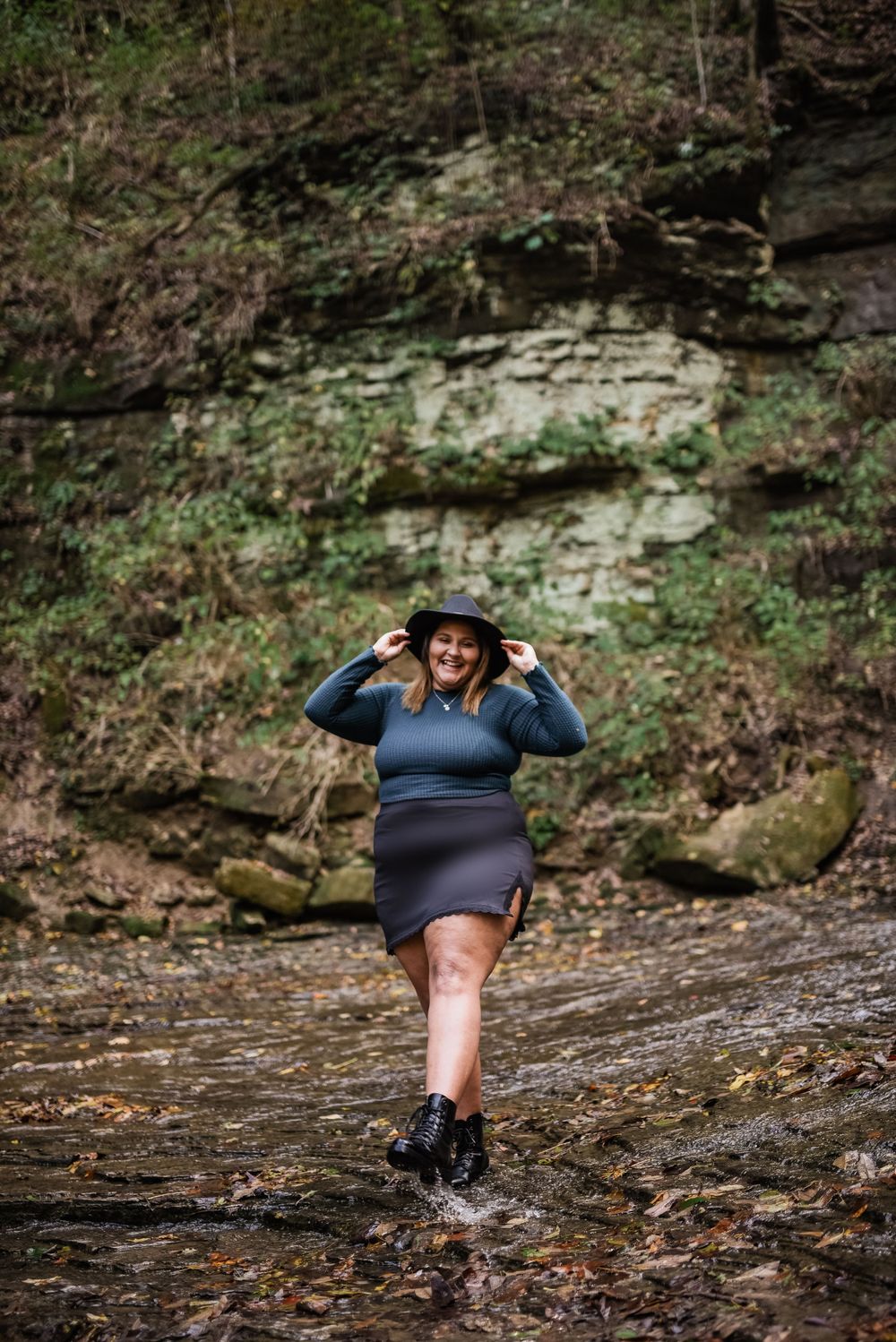 Person in blue top and hat poses dramatically on wet rocks.