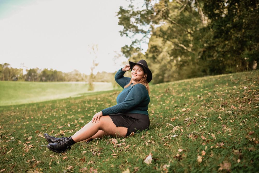 Figure in dark clothing reclines on grassy hillside during golden hour.
