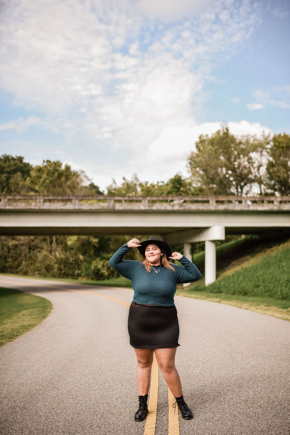 Person in blue top poses playfully on paved path under bright sky.
