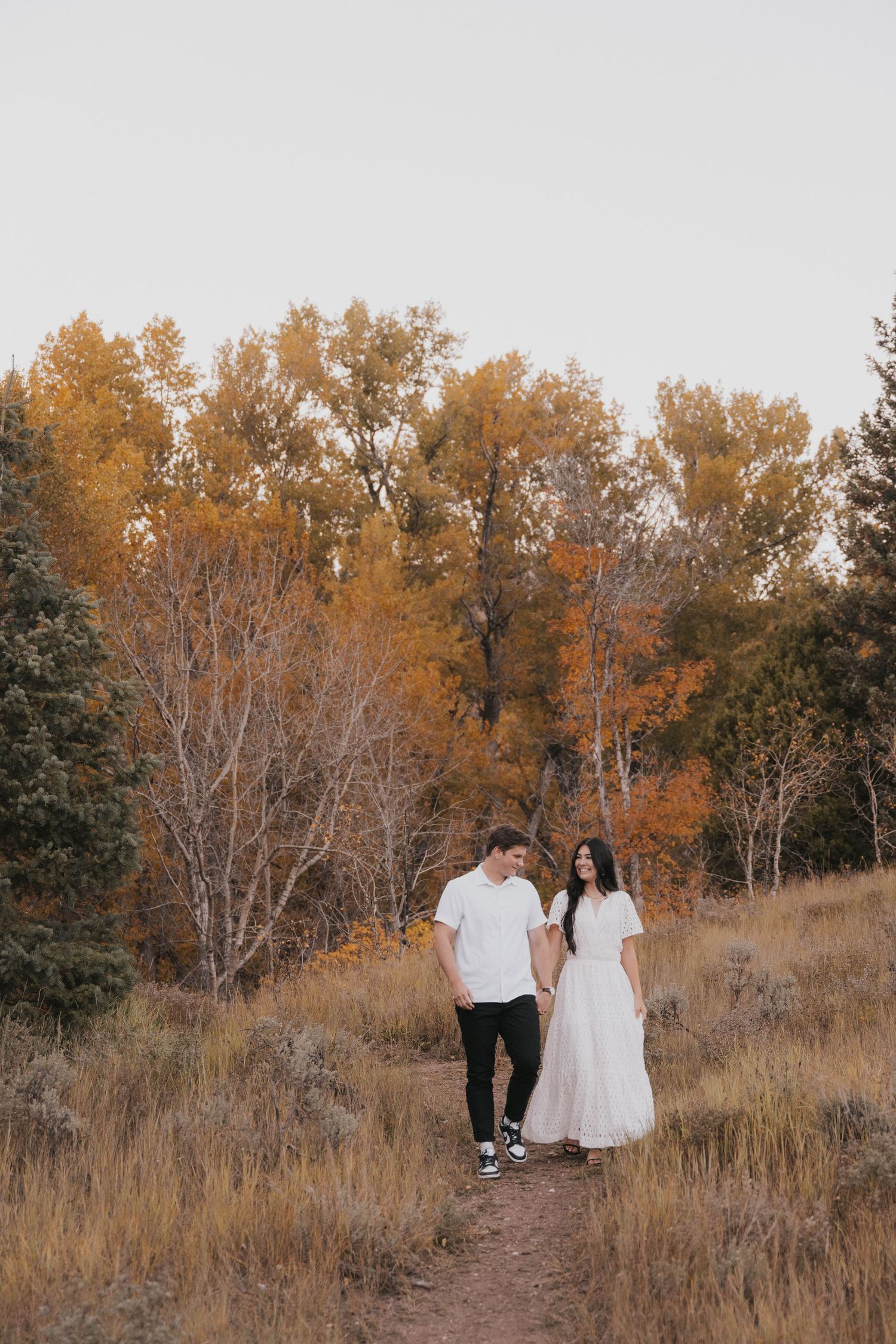 Couple walks in the fall leaves during their engagement session in American Fork Canyon,