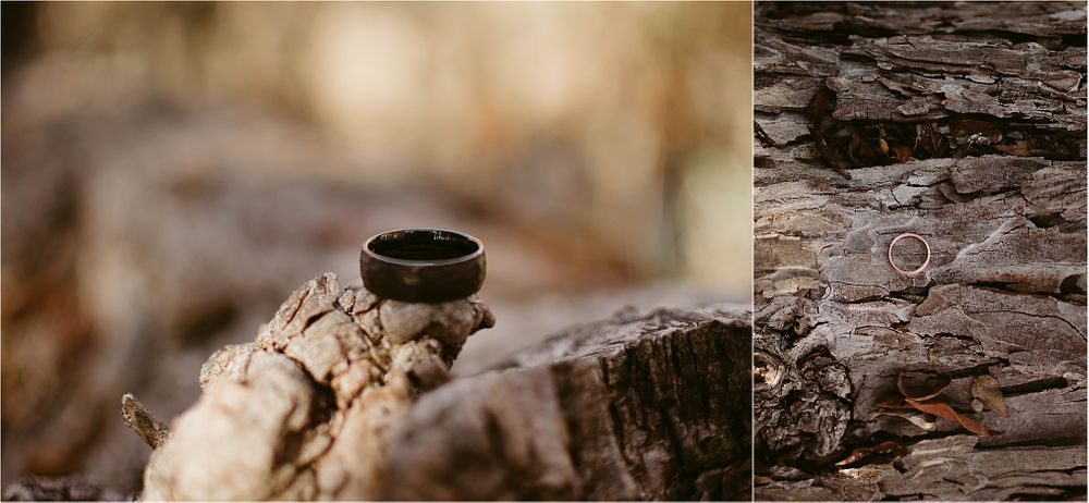 Black ring resting on natural wood with carved initials visible on bark surface.