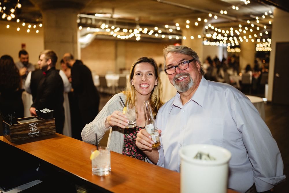 Guests enjoying drinks at a wooden bar under string lights at an indoor reception.