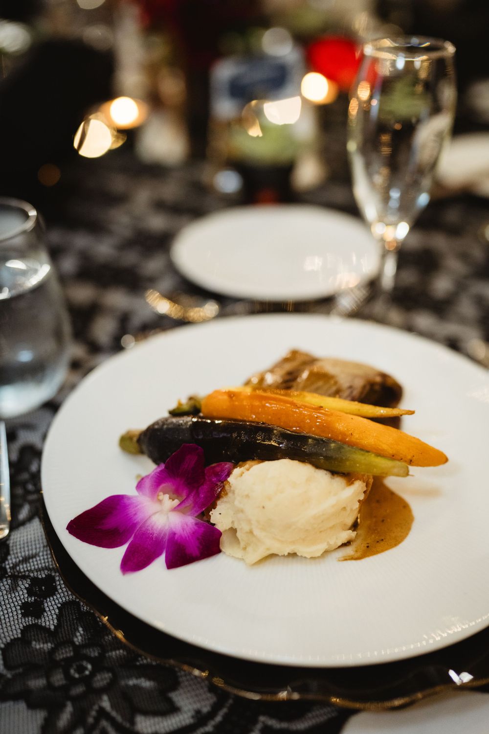 Elegant plated dinner with roasted vegetables, mashed potatoes and a purple orchid garnish.