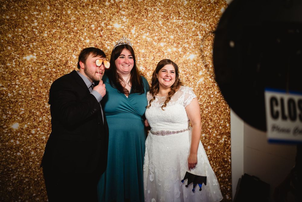 Three guests pose for a photo against a sparkly gold sequin backdrop at a wedding.
