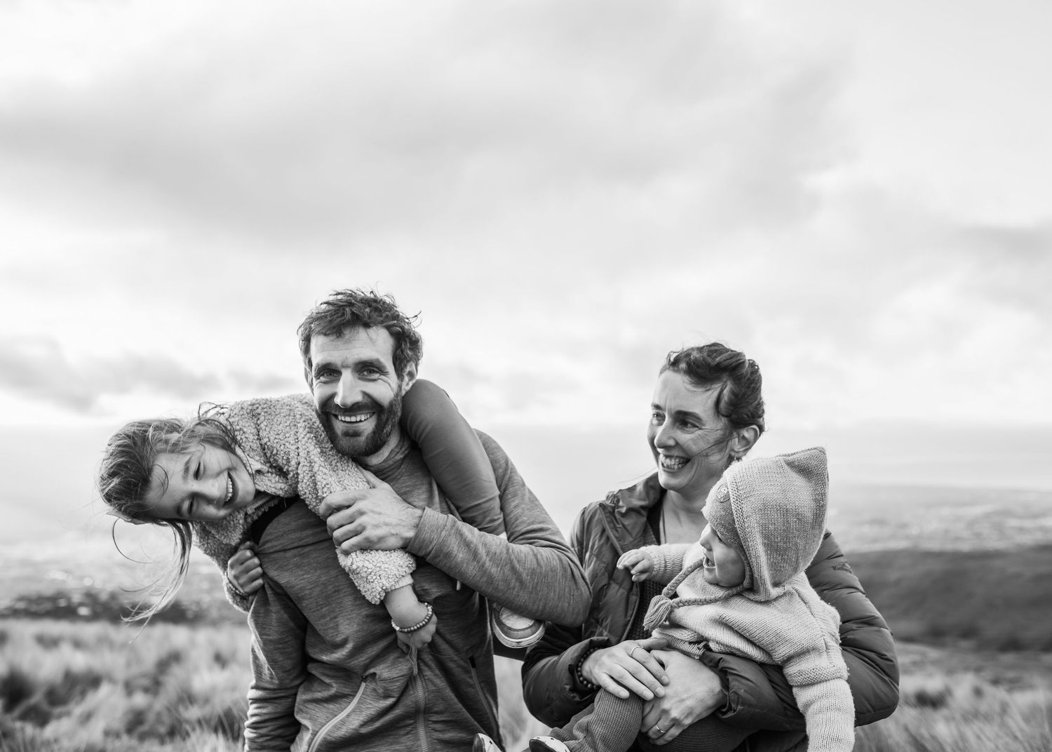 Playful black and white family portrait of adults and children laughing together outdoors.