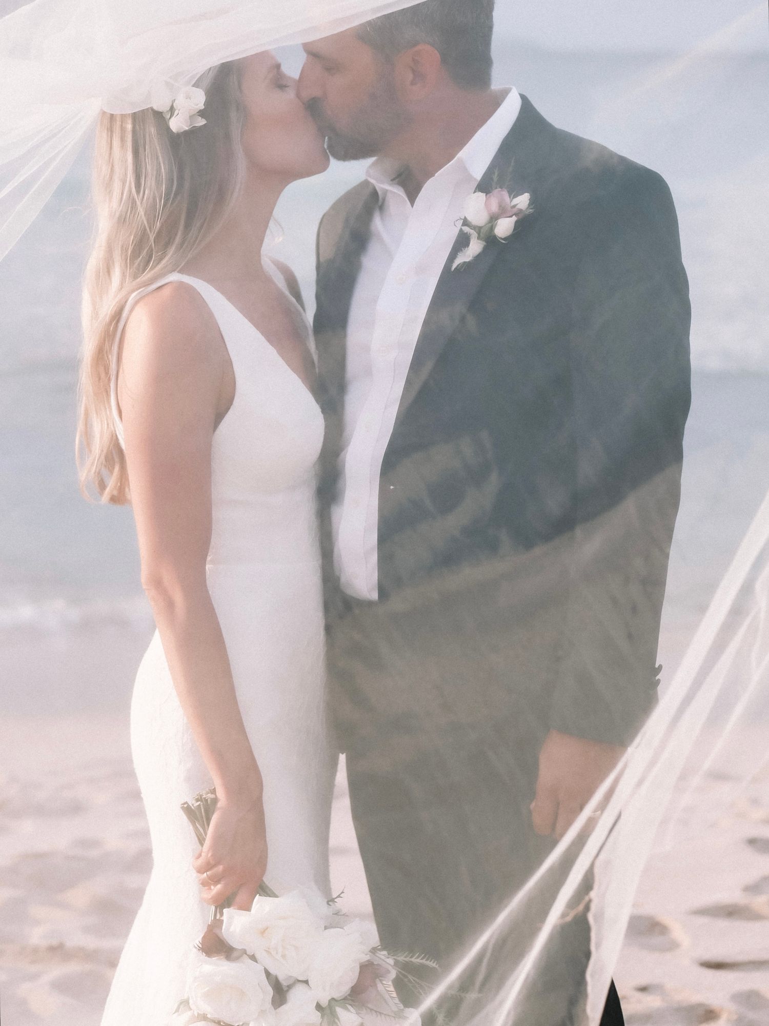 Elegant beach wedding photo with flowing white veil catching the breeze.