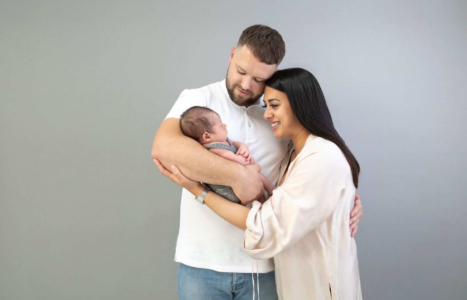 Family Photo shoot, Mum & dad gazing down at their cradled little boy in grey knitted outfit, grey background