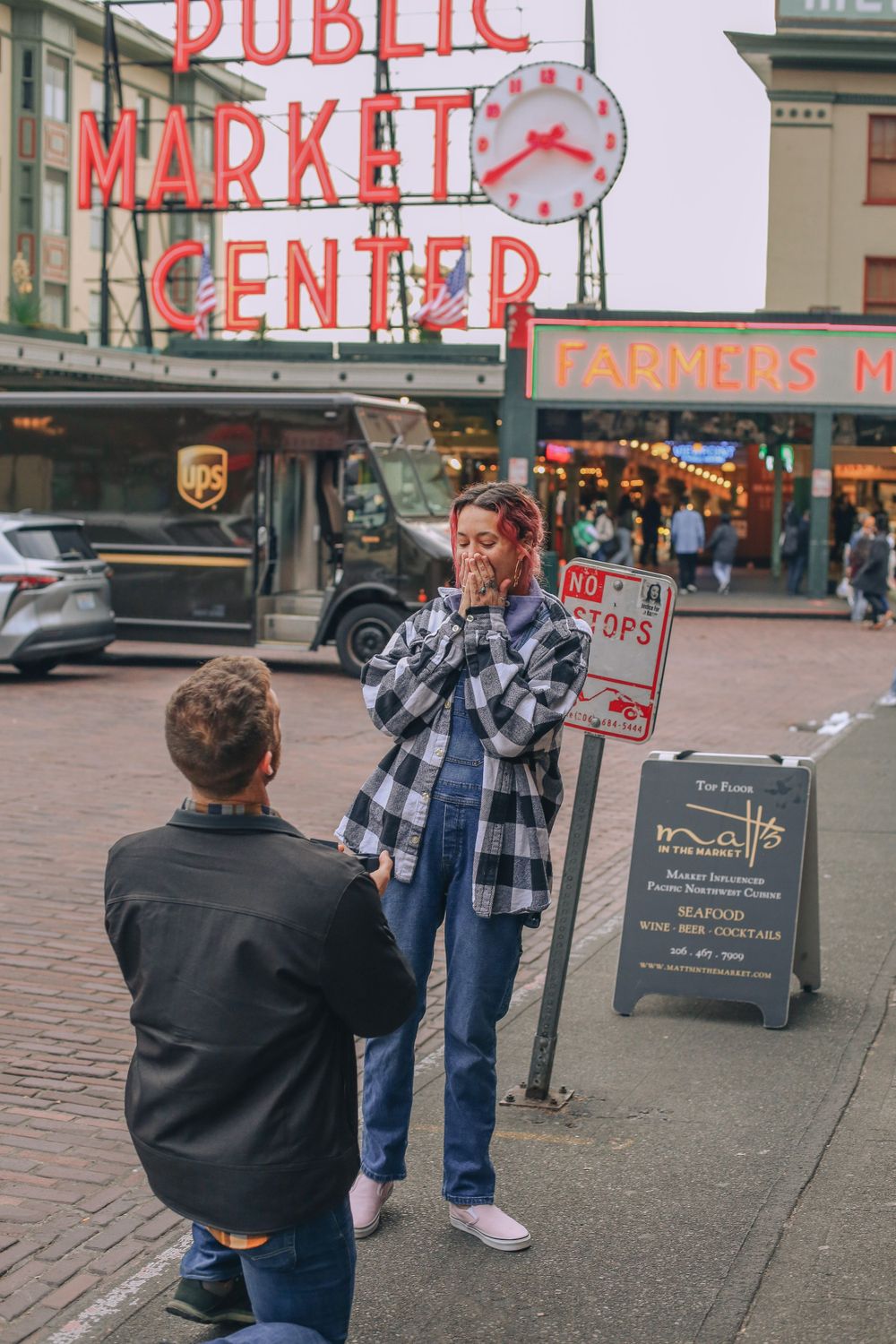 A proposal scene unfolds at Pike Place Market in Seattle as someone kneels in front of another person under the iconic sign. Spokane Liberty