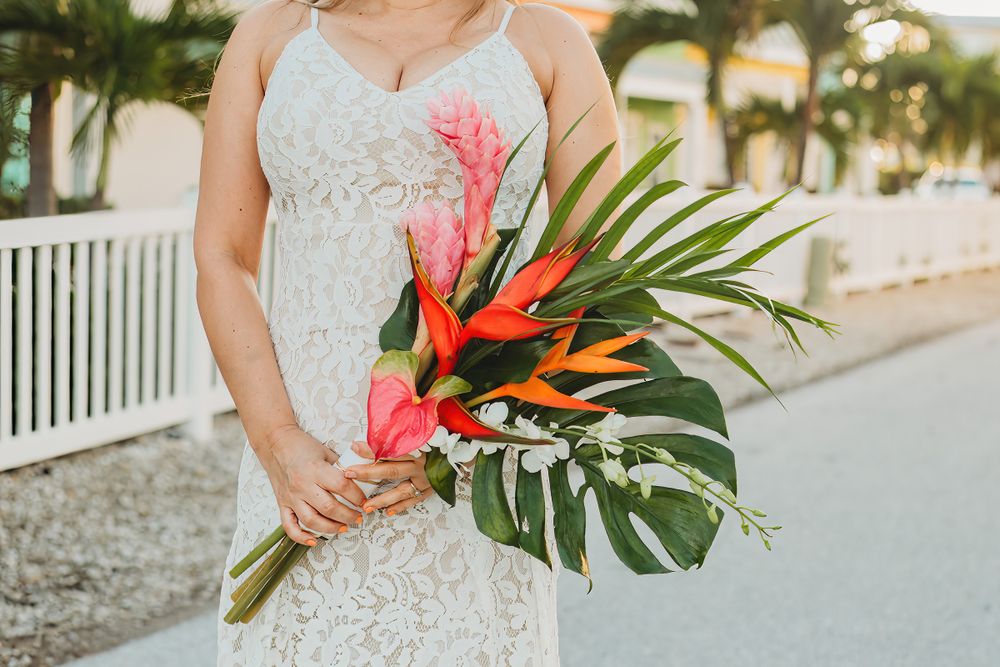A couple in wedding attire holding tropical flowers against a beach resort backdrop.