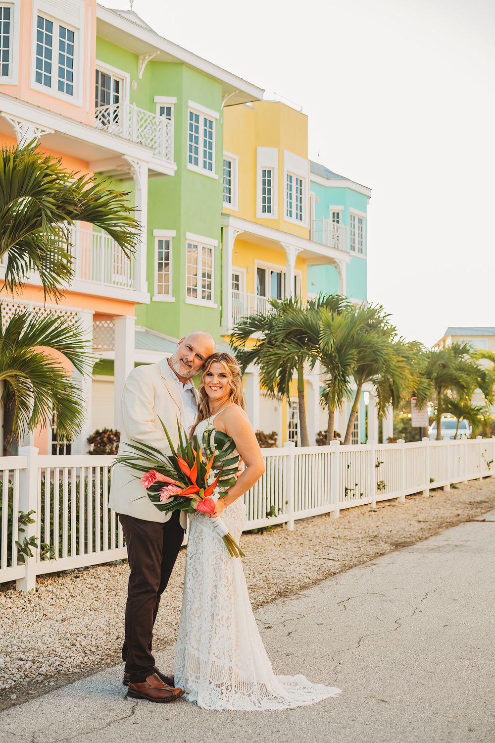 Couple posing in front of pastel-colored beach houses with tropical flowers.
