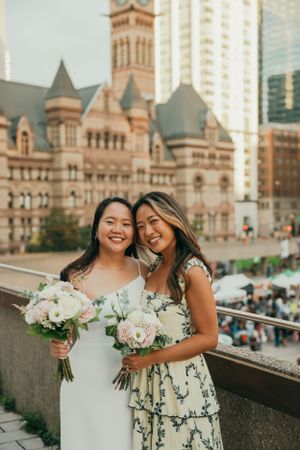 Two friends pose with bouquets in front of Toronto's historic Old City Hall building.