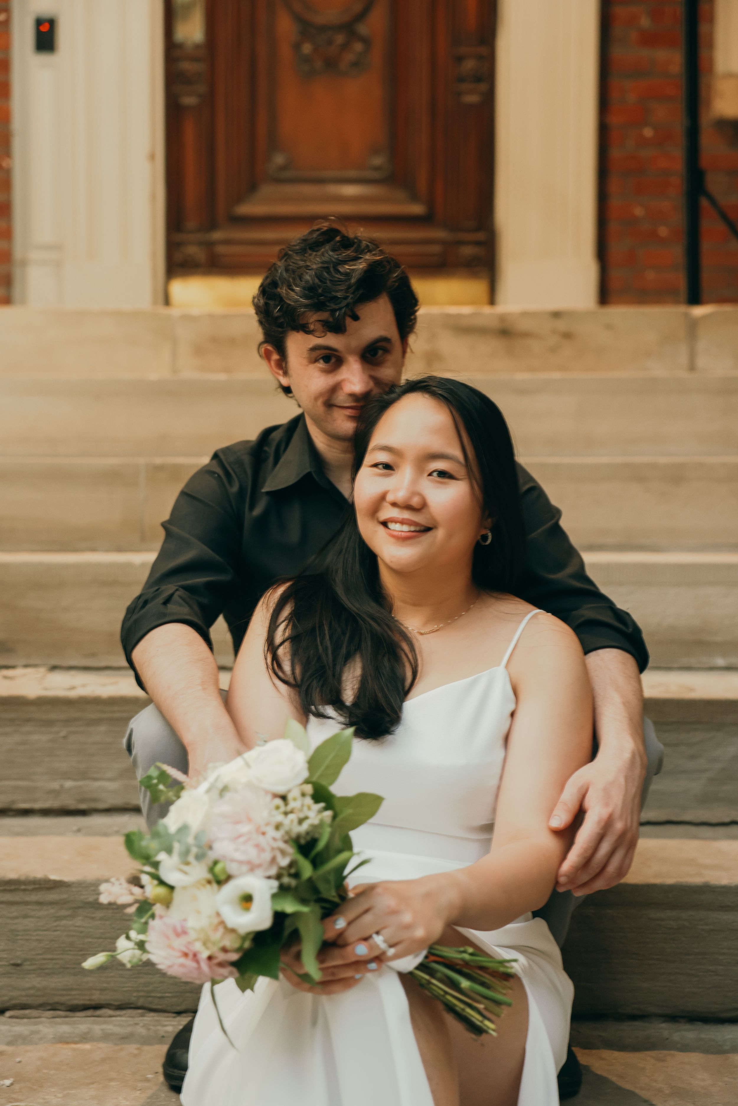 A happy couple poses together on stone steps in front of a vintage wooden door.