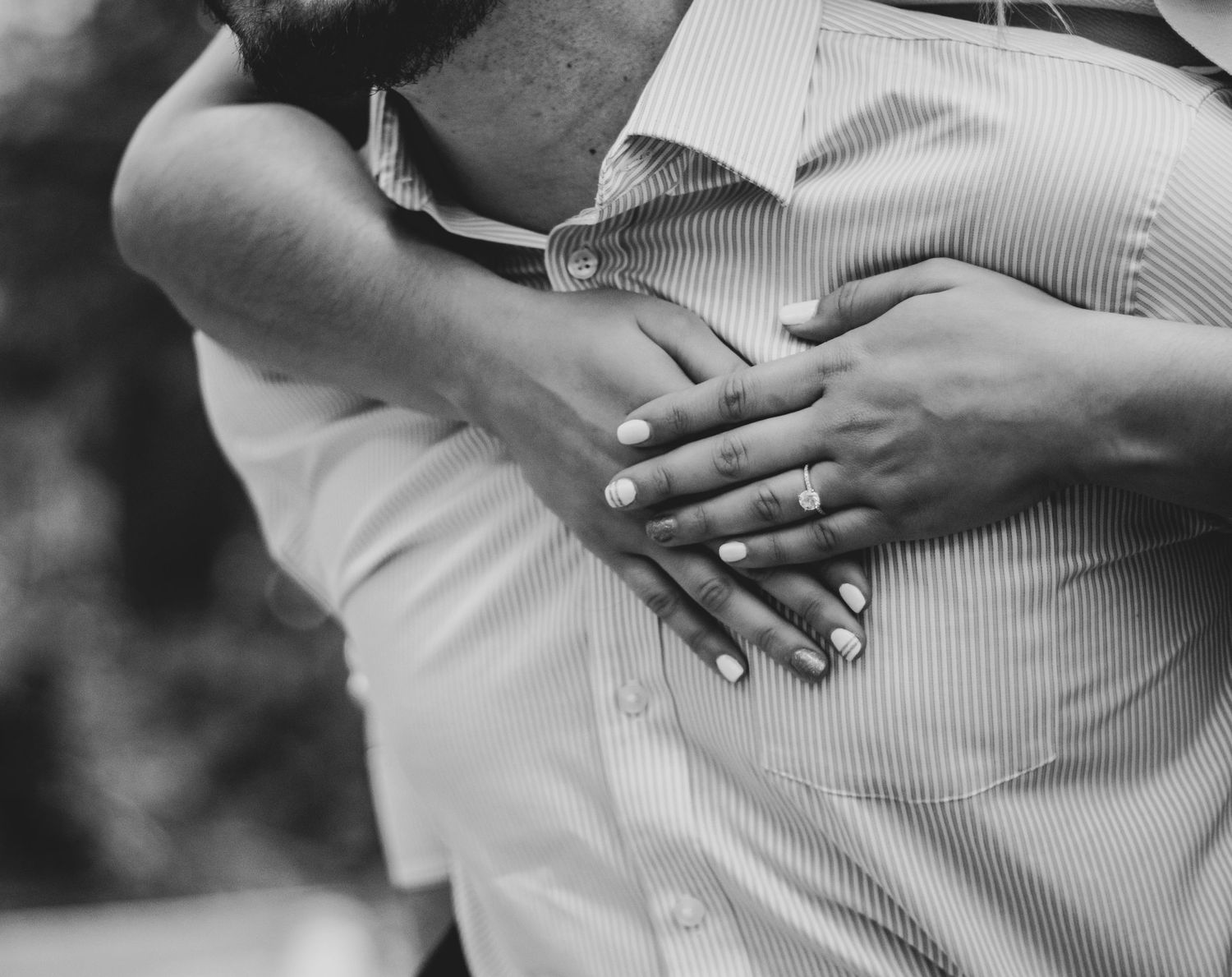 Close-up black and white shot of hands with engagement ring on a pinstripe shirt.