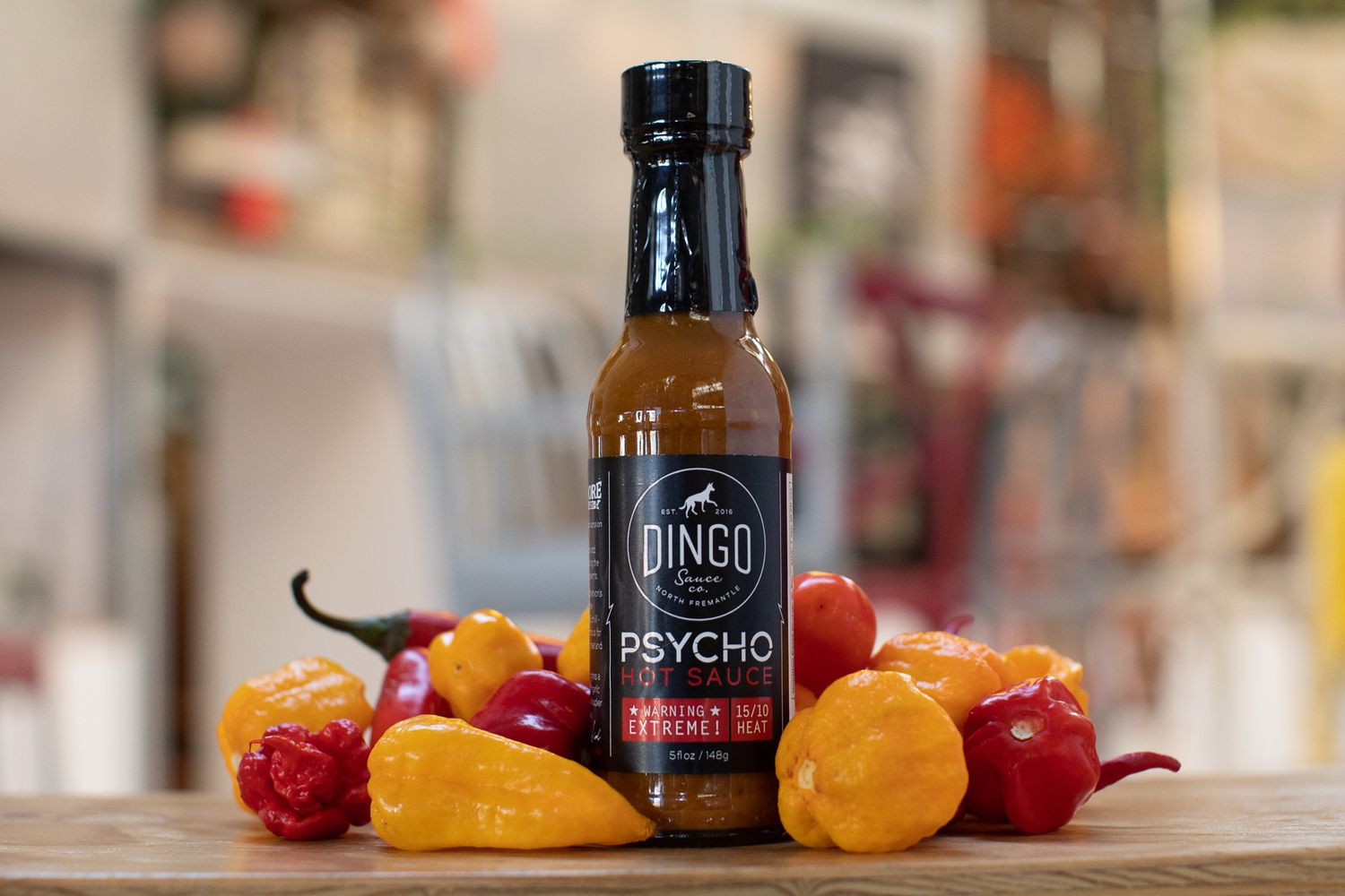 A bottle of Bingo Psycho hot sauce displayed with colorful fresh chili peppers on a wooden surface.
