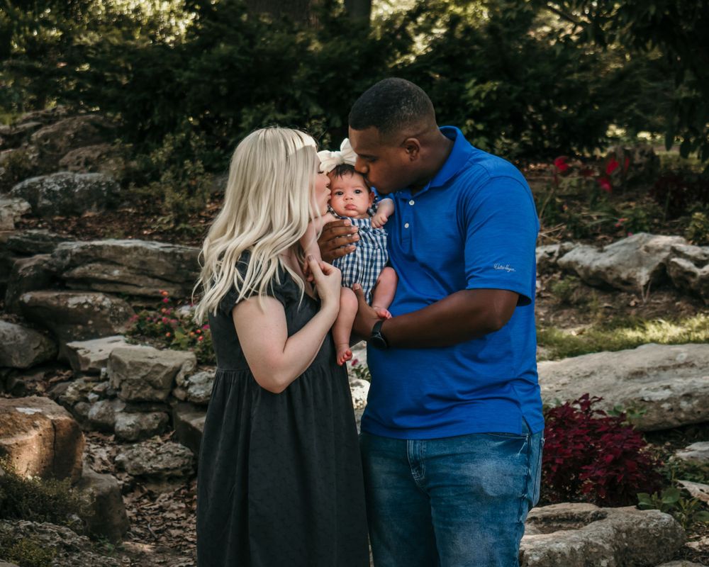 A couple both lean in to steal a kiss from their newborn's cheeks