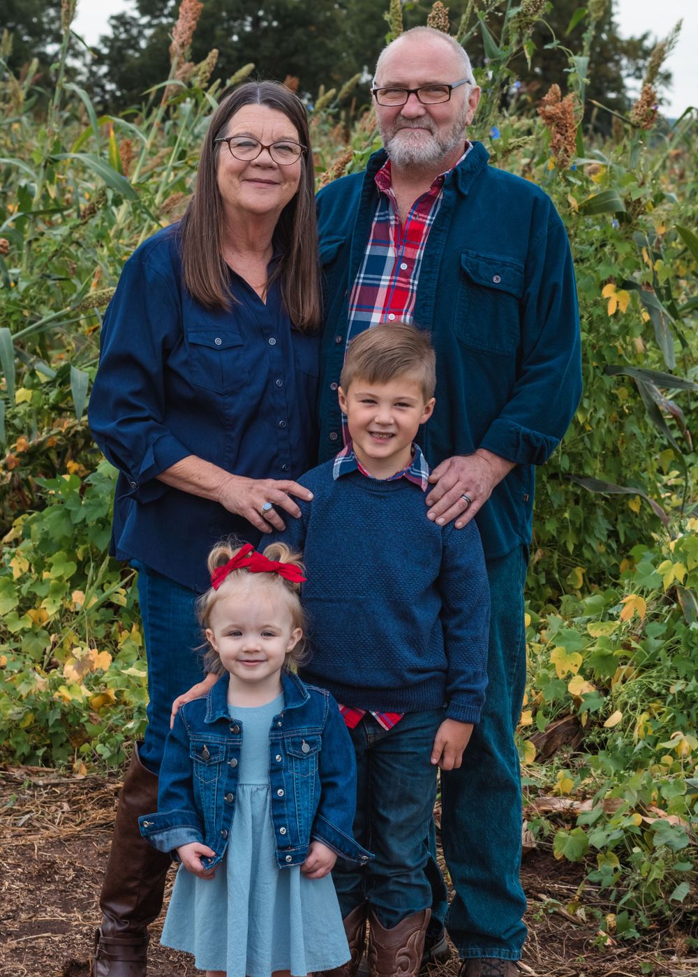 Two grandparents and their grandchildren smiling in front of a corn maze