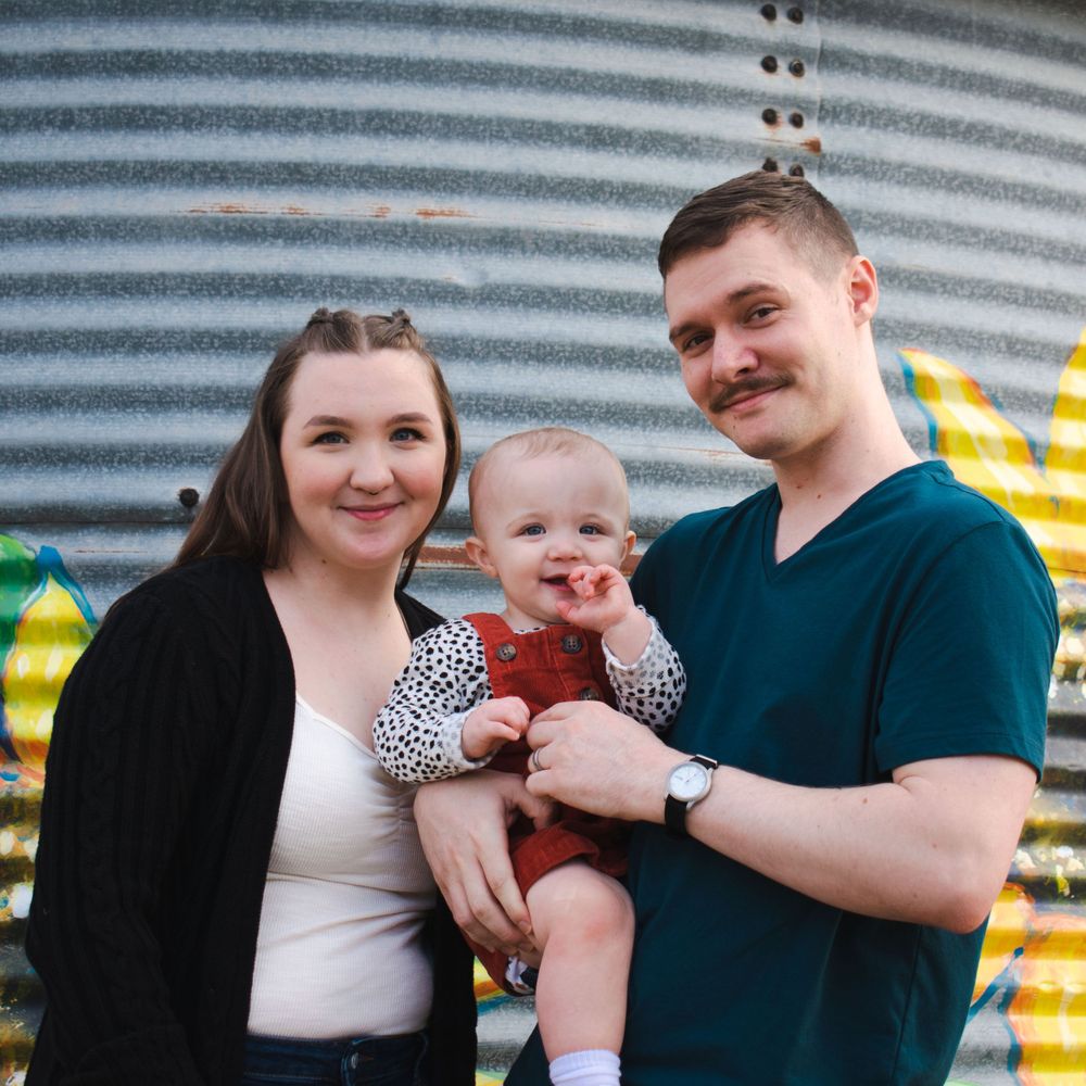 A young couple takes a moment to pose with their baby at a pumpkin patch