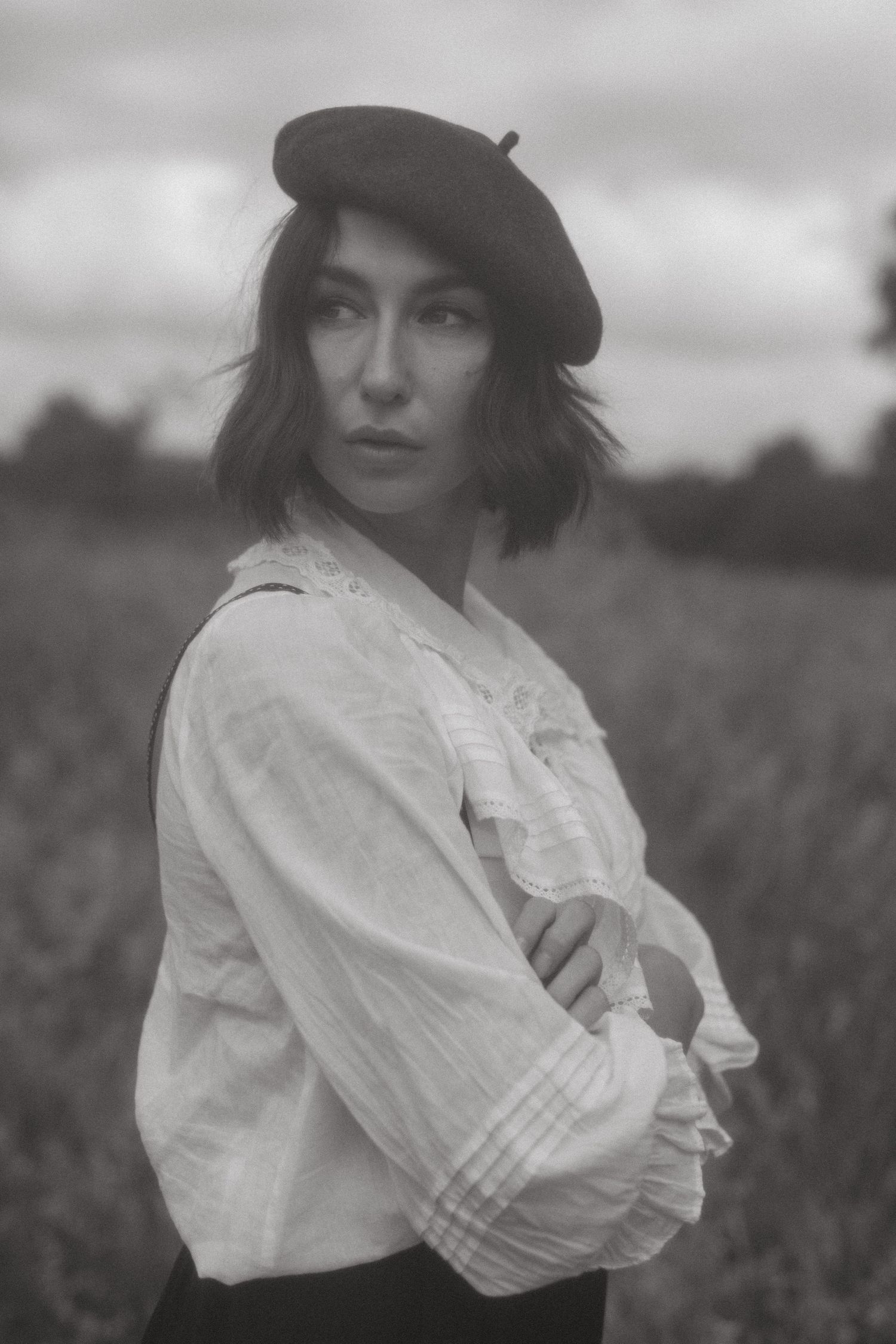 Black and white portrait series of woman in white vintage blouse and hat in a field.