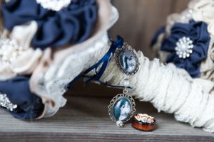 bride's and groom's rings lay stacked on a shelf, beside them the brides button bouquet is placed. An open locket is attached to the bouquet