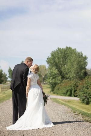 bride and groom walk holding hands down a gravel country road. They stop for a brief kiss.