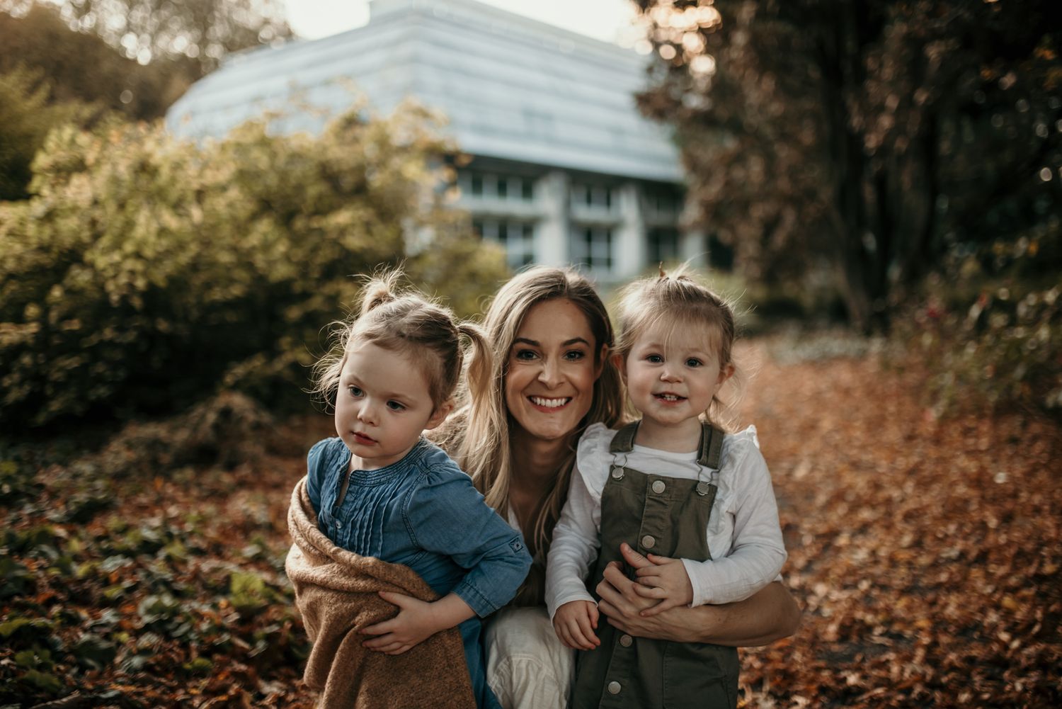 A joyful family moment captured in autumn foliage with warm golden tones and a modern building in the background.