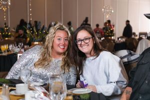Holiday party guests mingling at tables with festive Christmas decorations.