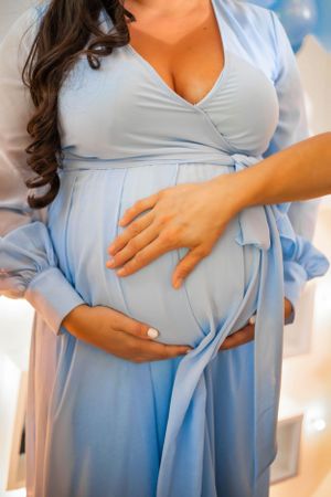 A person wearing a light blue flowing dress cradles their pregnant belly.