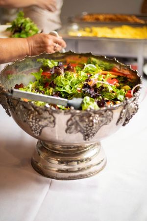 An elegant silver serving bowl filled with fresh salad and colorful vegetables.