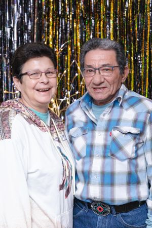A couple poses against a sparkly gold and black backdrop at a holiday party.
