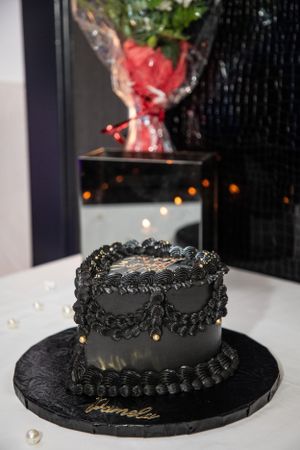 Black frosted cake with decorative piping sits on a dark plate against a dark background.