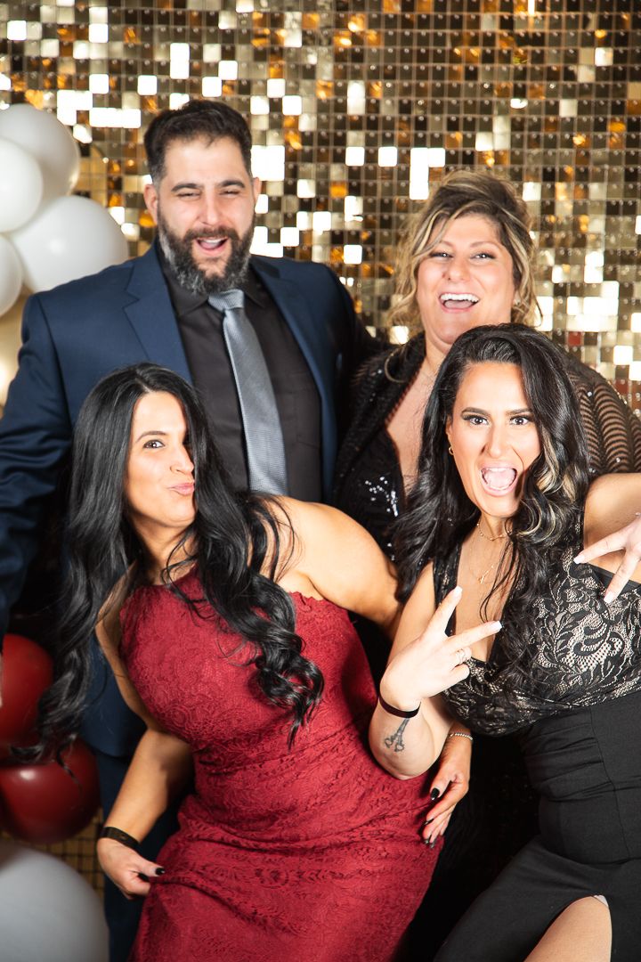 Group poses playfully against a gold sequin backdrop with balloons at a formal event.