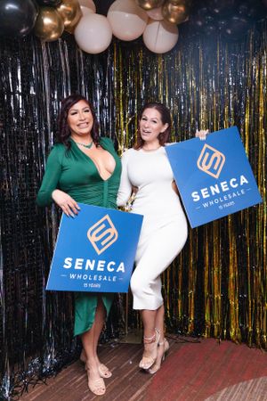 Two attendees posing with Seneca Wholesale signs against a metallic fringe backdrop.