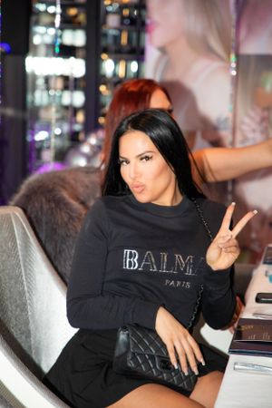 Guest wearing black Balmain sweater lounging on gray couch at social gathering.