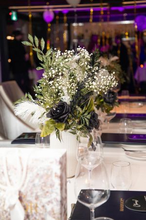 Elegant table setting with black and white floral centerpiece arrangements and wine glasses under purple ambient lighting.