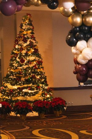Elegant Christmas trees with lights and decorations alongside purple and gold balloon arrangements.