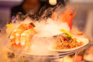 Dramatic smoky presentation of shrimp dish on elegant white plate.