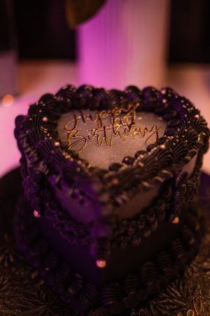 Elegant chocolate birthday cake with decorative piping and 'Happy Birthday' text in purple lighting.