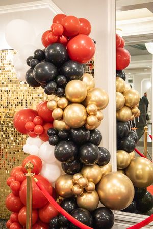 Luxurious balloon arch featuring red, gold, black, and white balloons against a metallic wall.