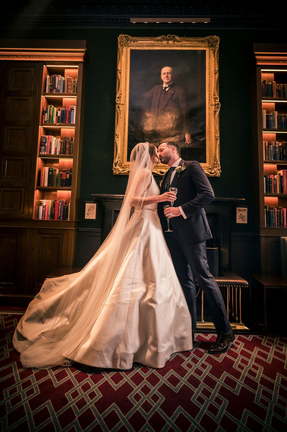 Bride and groom kissing in an elegant library in The Shelbourne Hotel with bookshelves and a classic portrait painting behind them.