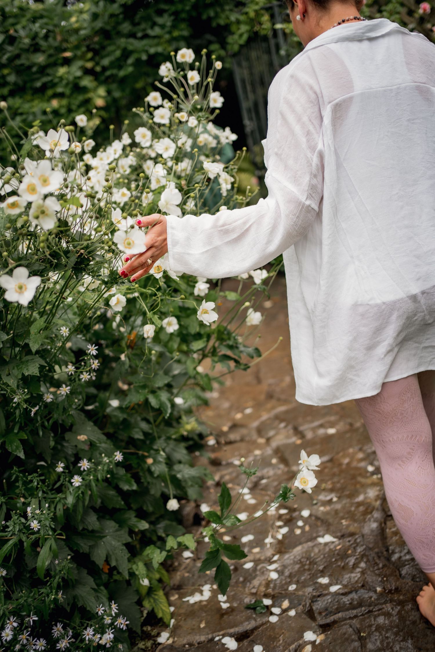 Person in white shirt reaching to touch blooming white flowers in a garden.