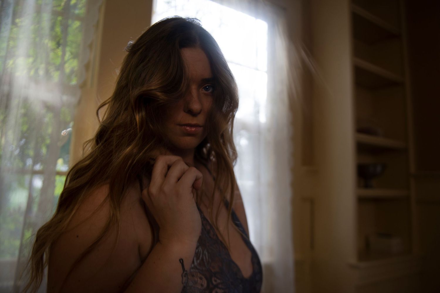 Atmospheric backlit portrait in moody interior setting with window light.