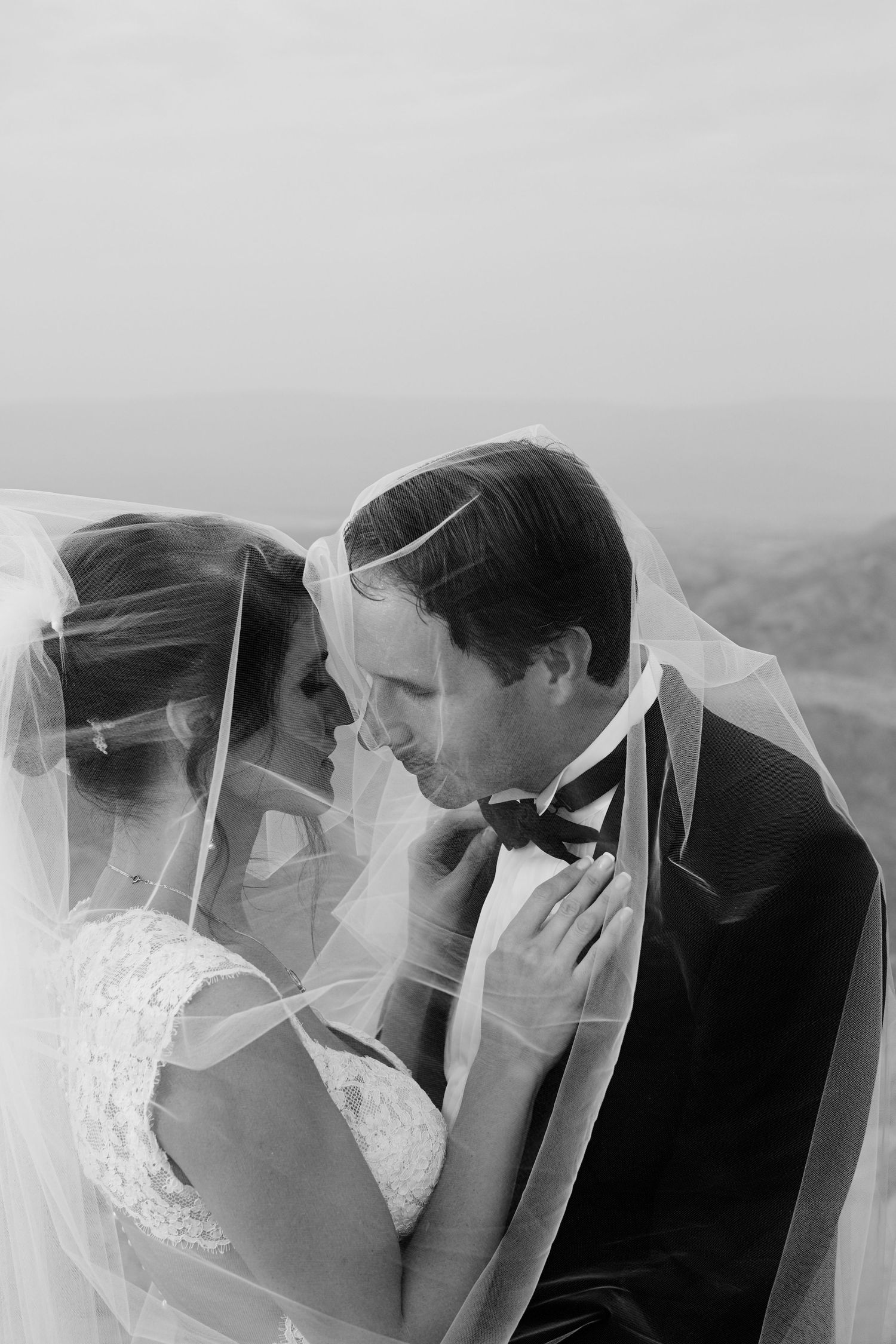 Romantic wedding portrait of couple embracing under a sheer veil against a misty backdrop.