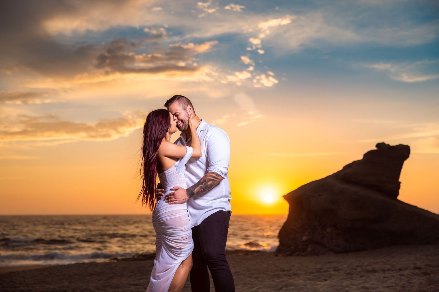 Romantic couple embracing on beach during dramatic orange sunset.