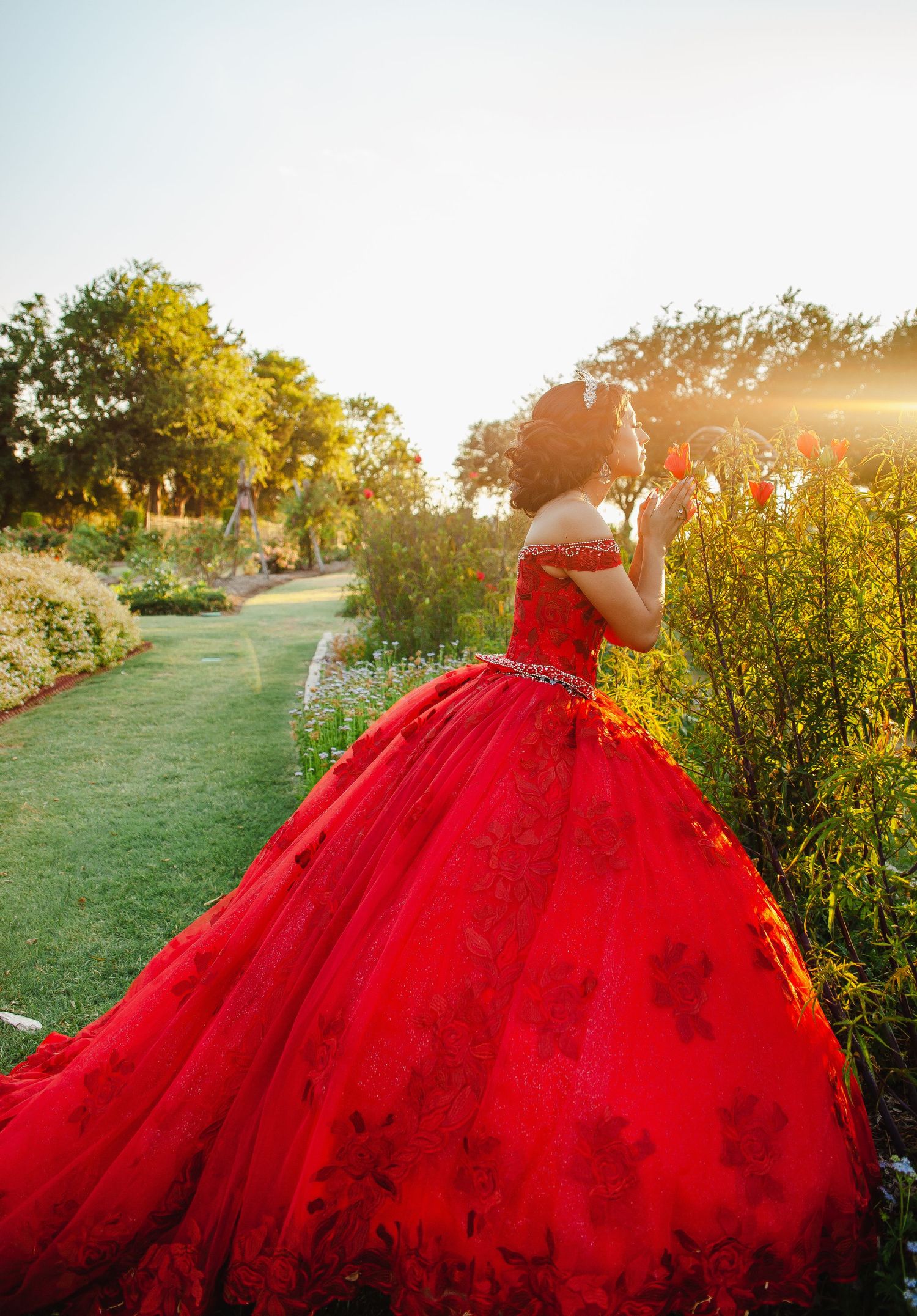 Dramatic red ballgown photographed in golden sunset light among garden flowers.