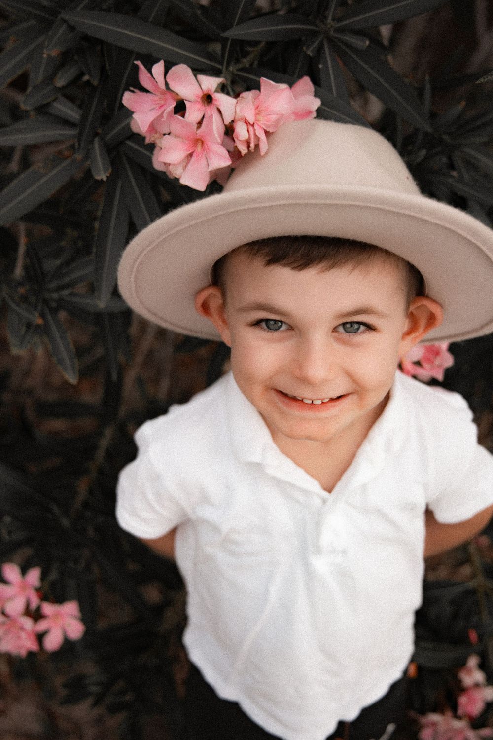 Young child wearing white hat with pink flowers smiles at camera.
