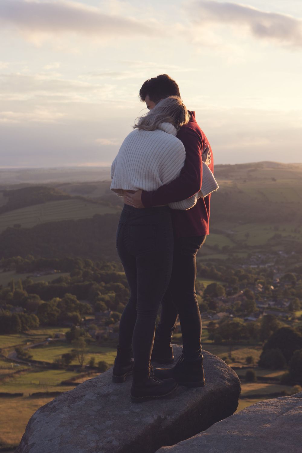 Couple embracing while standing on rocky overlook during sunset. Curbar Edge.