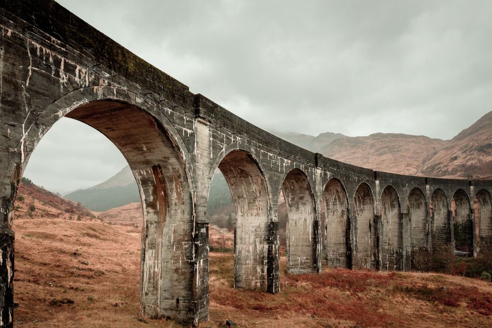 Historic stone railway viaduct with multiple arches spans across a rugged highland landscape. Harry Potter.