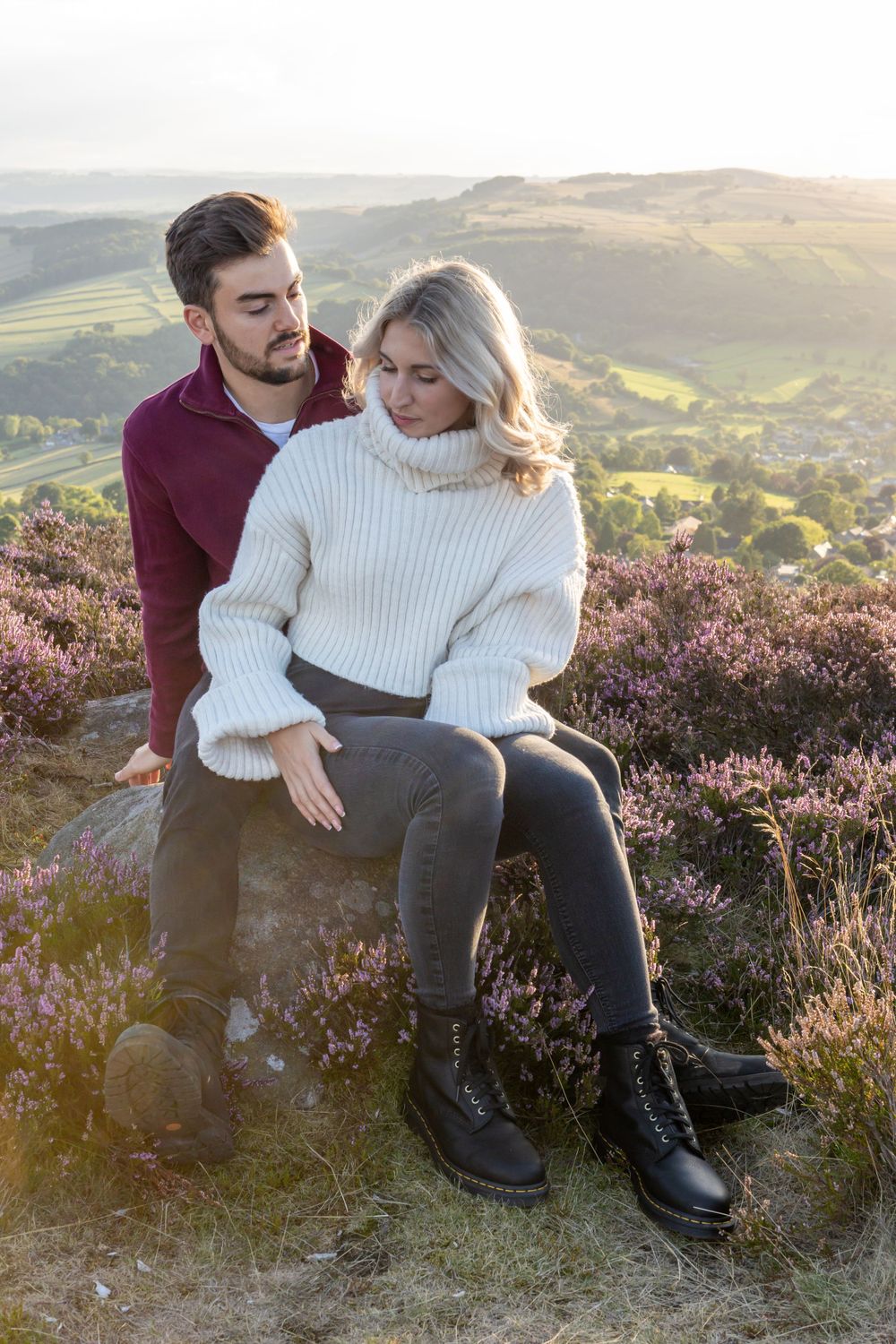 Couple in casual sweaters sitting on hillside overlooking scenic valley at sunset. Curbar Edge.