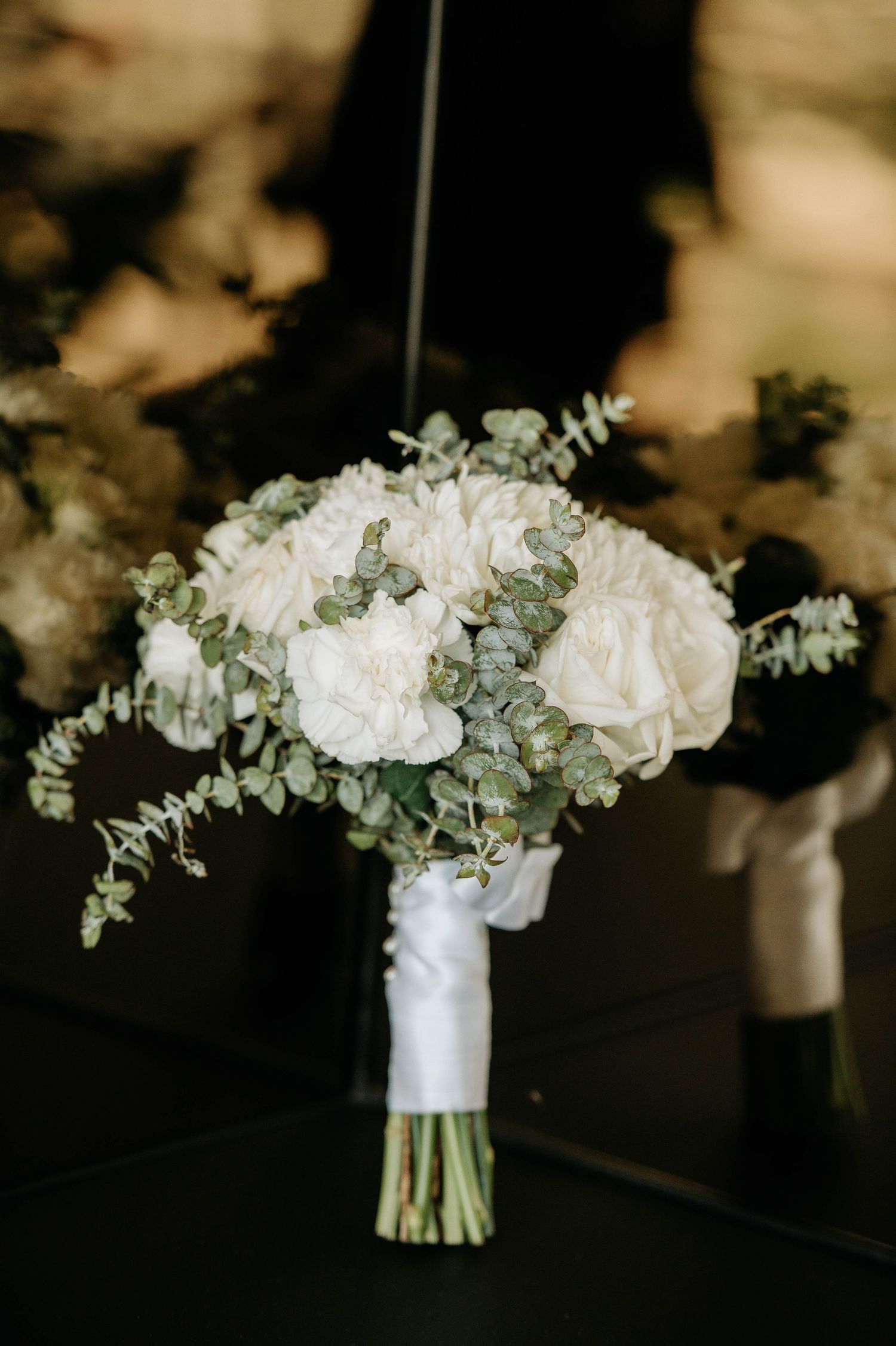 Elegant white wedding bouquet with roses and eucalyptus wrapped in silk ribbon.